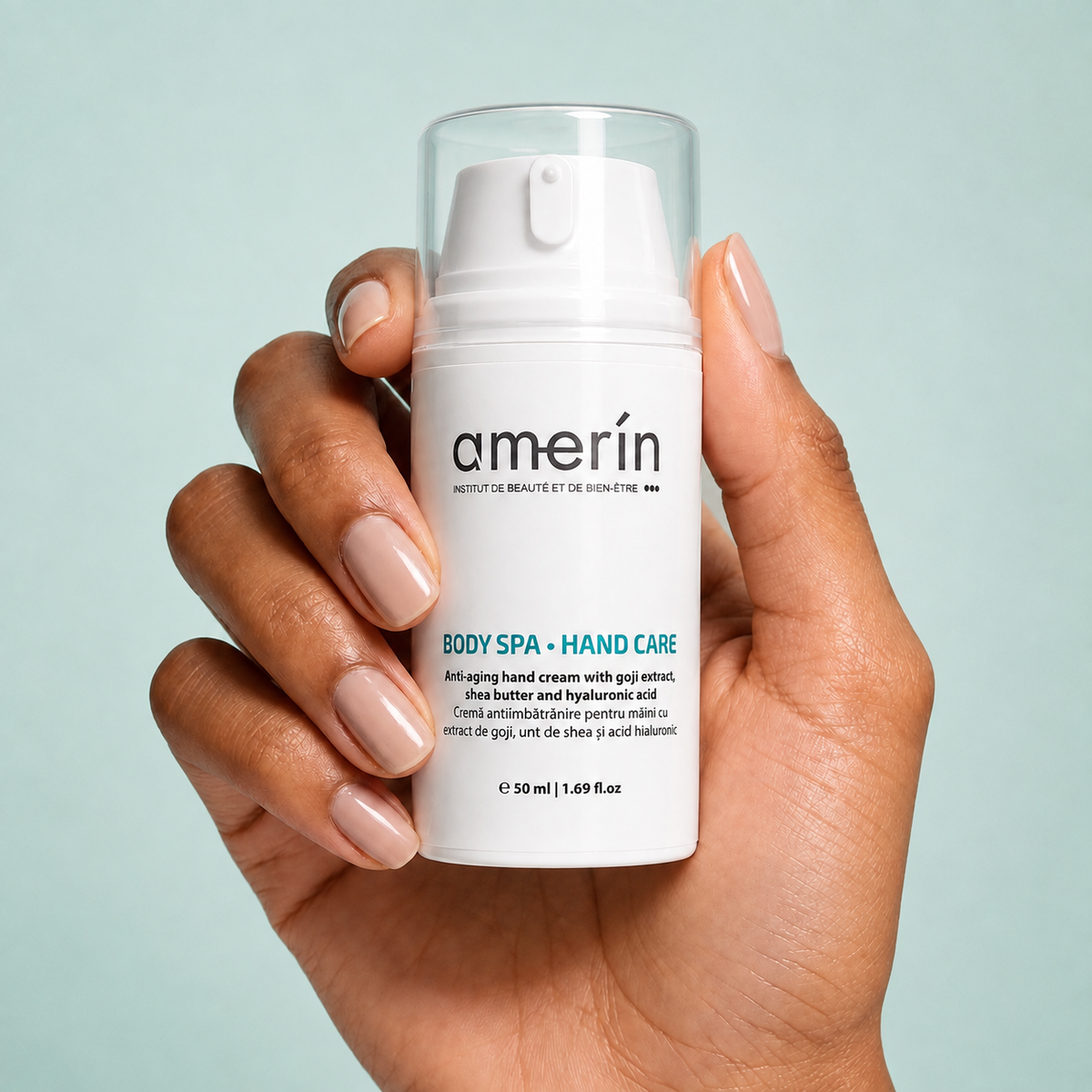 A hand with manicured nails holds a white Amerín anti-aging hand cream pump bottle against a light blue background.