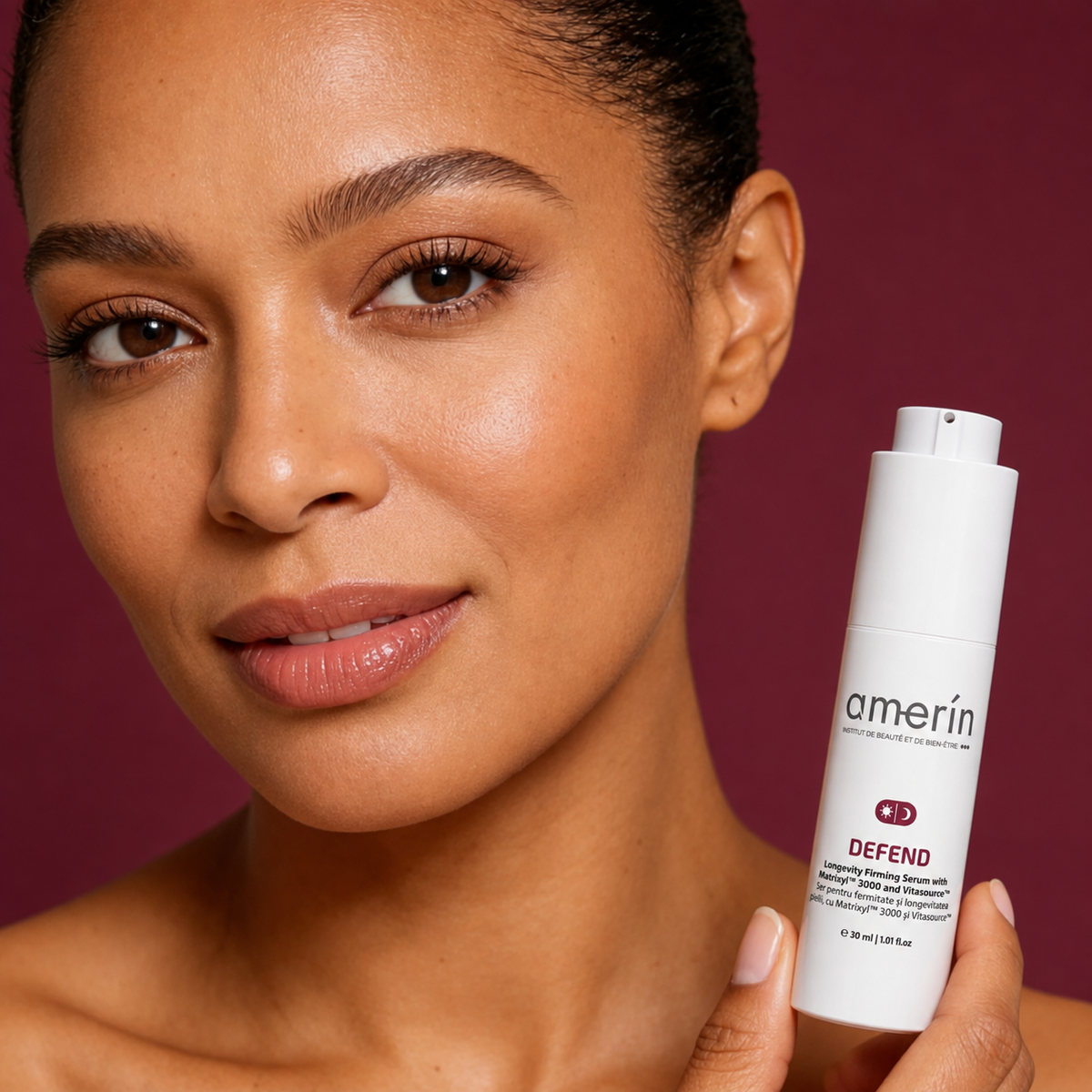 A close-up of a woman holding a white Amerin DEFEND serum against a solid deep burgundy background.