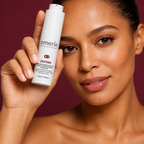 A close-up of a woman holding a white Amerin DDEFEND | Peptide Recovery Night Cream with Matrixyl™ 3000 and Sodium Hyaluronate cream bottle next to her face, set against a solid deep burgundy background.