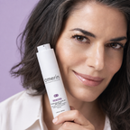 A woman holding a white Amerín Reborn hair restoration gel bottle against a solid lavender background.