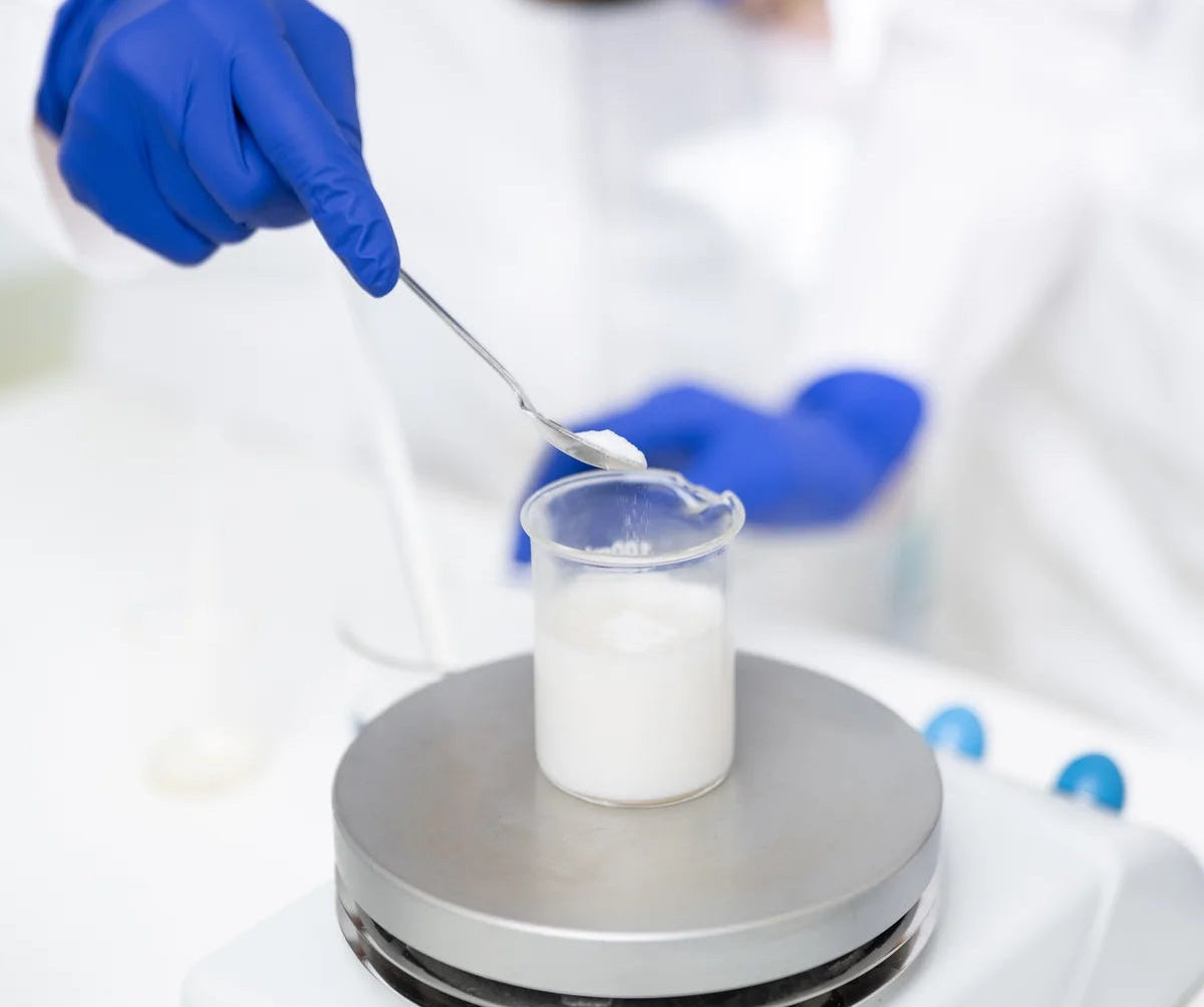 Person in a lab coat and gloves stirring a beaker with a hot plate in a laboratory setting.